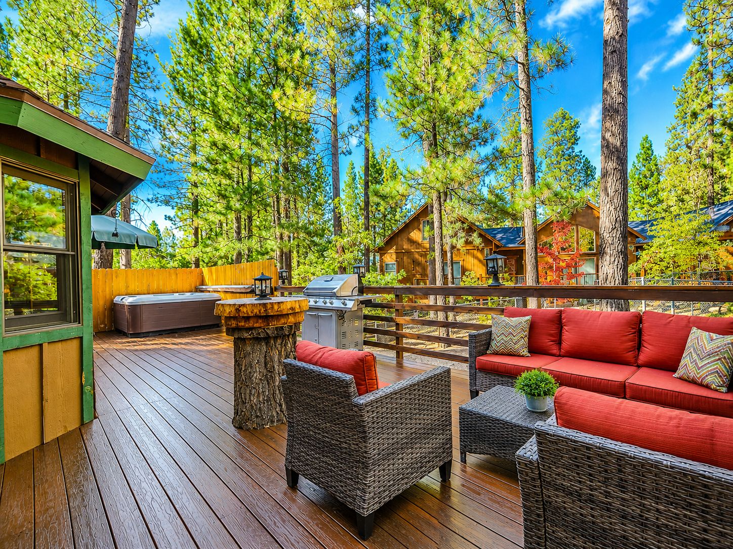 Una terraza de madera con mobiliario exterior, una parrilla y vistas del bosque circundante.