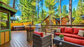 Una terraza de madera con mobiliario exterior, una parrilla y vistas del bosque circundante.