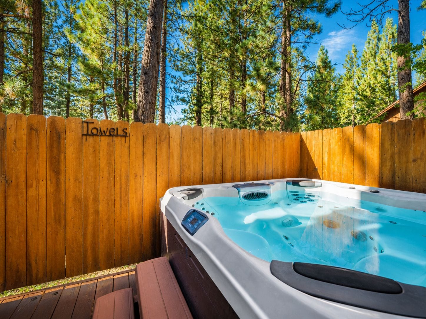 Ein Whirlpool in einem Holzdeckbereich, im Hintergrund ein Holzzaun mit der Aufschrift 'Towels'.