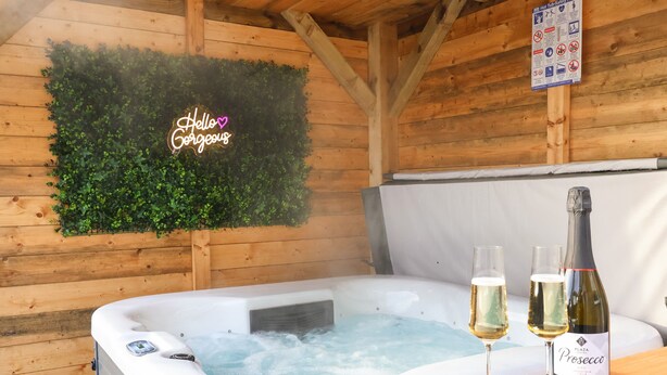 A hot tub with two glasses of Prosecco and a bottle on a wooden table, surrounded by wooden walls and a green wall decoration. - The Coastal Hideaway (Hornsea)