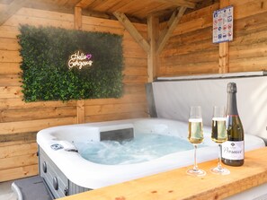 Un jacuzzi con dos copas de Prosecco y una botella sobre una mesa de madera, rodeado de paredes de madera y un adorno mural verde.