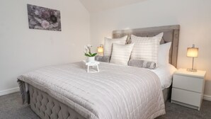 A neatly arranged bedroom with a large bed, a bedside table with a lamp, and a small white nightstand. - The Coastal Hideaway (Hornsea)