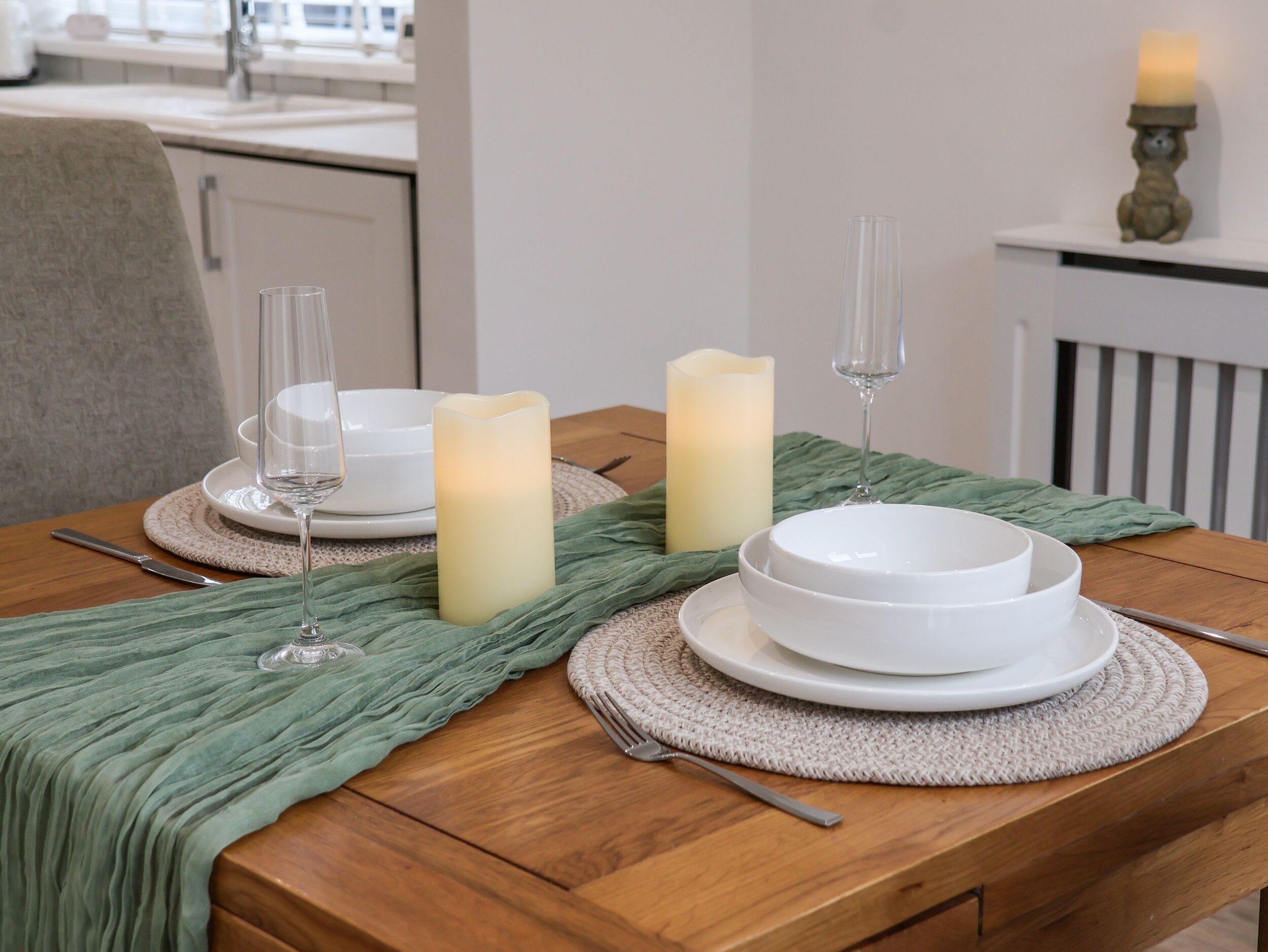 A dining table set with white plates, bowls, and cutlery, accompanied by candles and a green cloth.