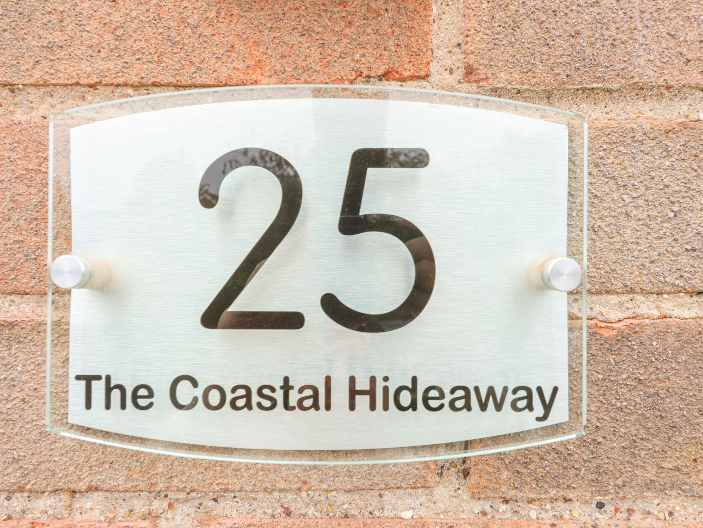 Une plaque indiquant le numéro de maison, portant le numéro 25 et l’inscription « The Coastal Hideaway », fixée à un mur de briques.