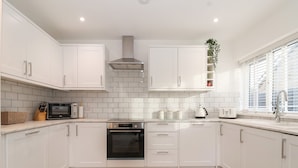 A modern kitchen with white cabinets, a built-in oven, a microwave, and a kettle. - The Coastal Hideaway (Hornsea)