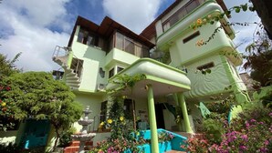 Um edifício de dois andares com fachada verde clara, uma fonte no jardim e uma escadaria que dá acesso à entrada.