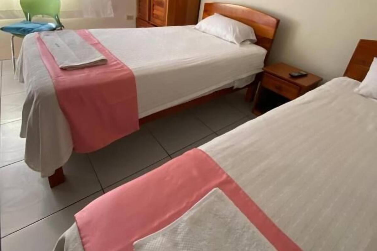 Ein Hotelzimmer mit zwei Betten, einem Holzschrank, einem grünen Stuhl und einem Fenster mit Vorhängen.