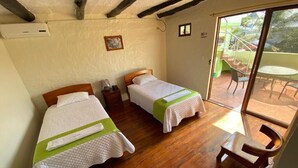 Quarto com duas camas, piso de madeira, porta de vidro deslizante para área externa e uma pequena mesa com cadeiras.