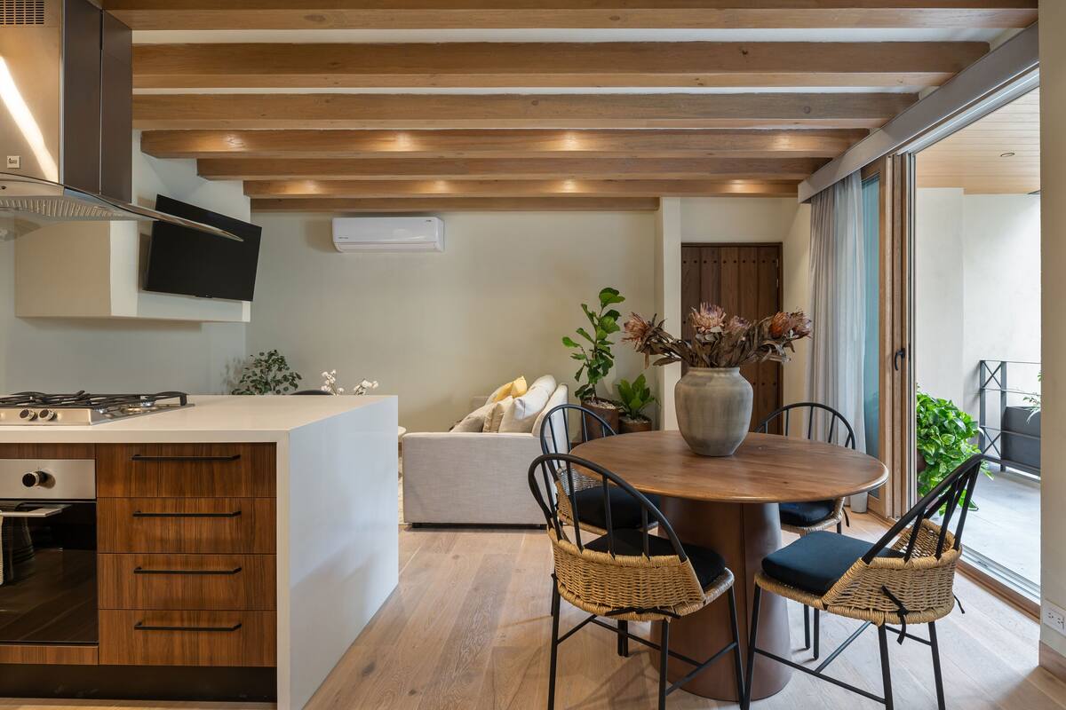 Une cuisine moderne dotée d’une cuisinière intégrée, de meubles en bois et d  ’un coin repas avec des chaises en osier et une table en bois.