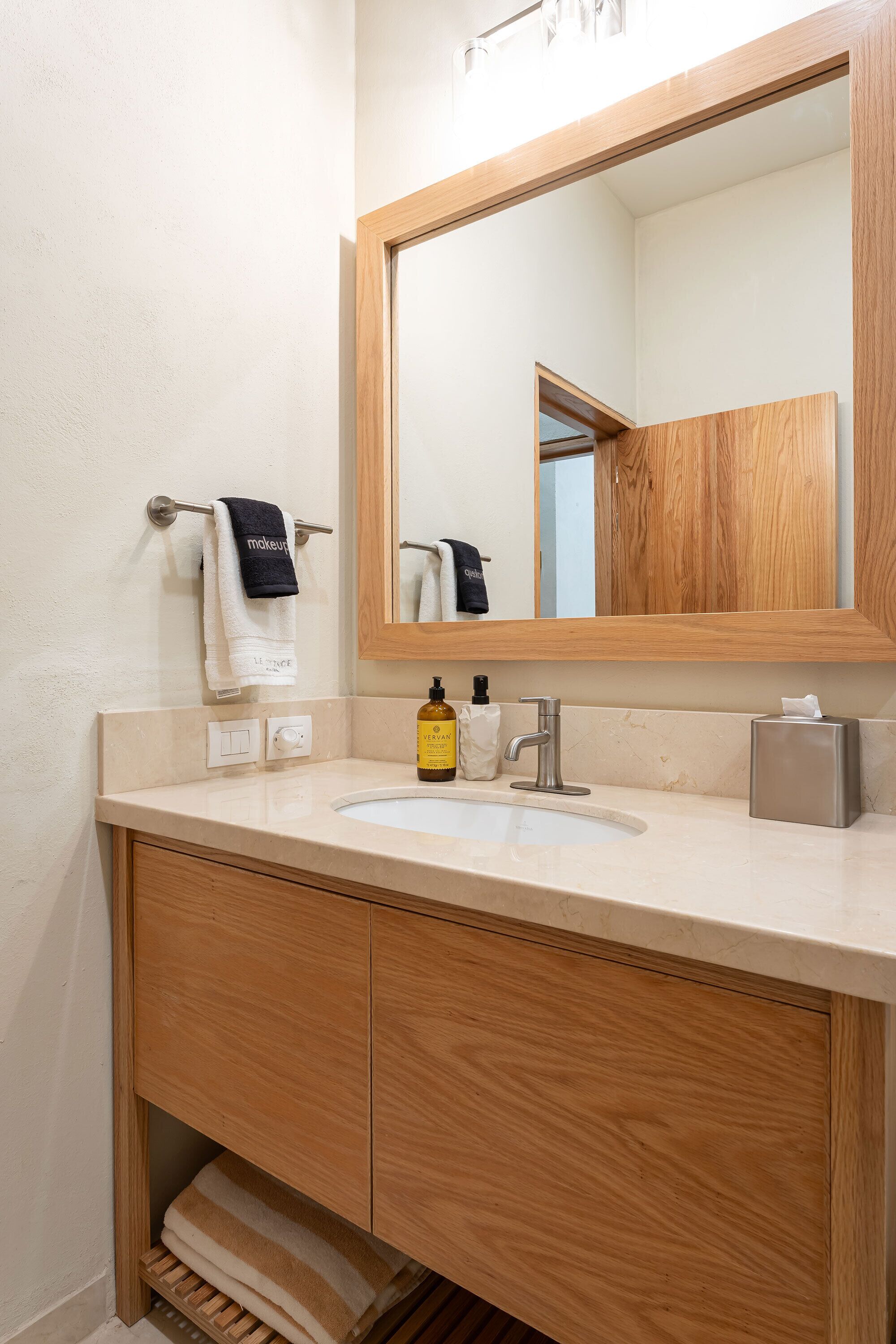 Un baño con tocador de madera, lavamanos, espejo y barra para toallas.