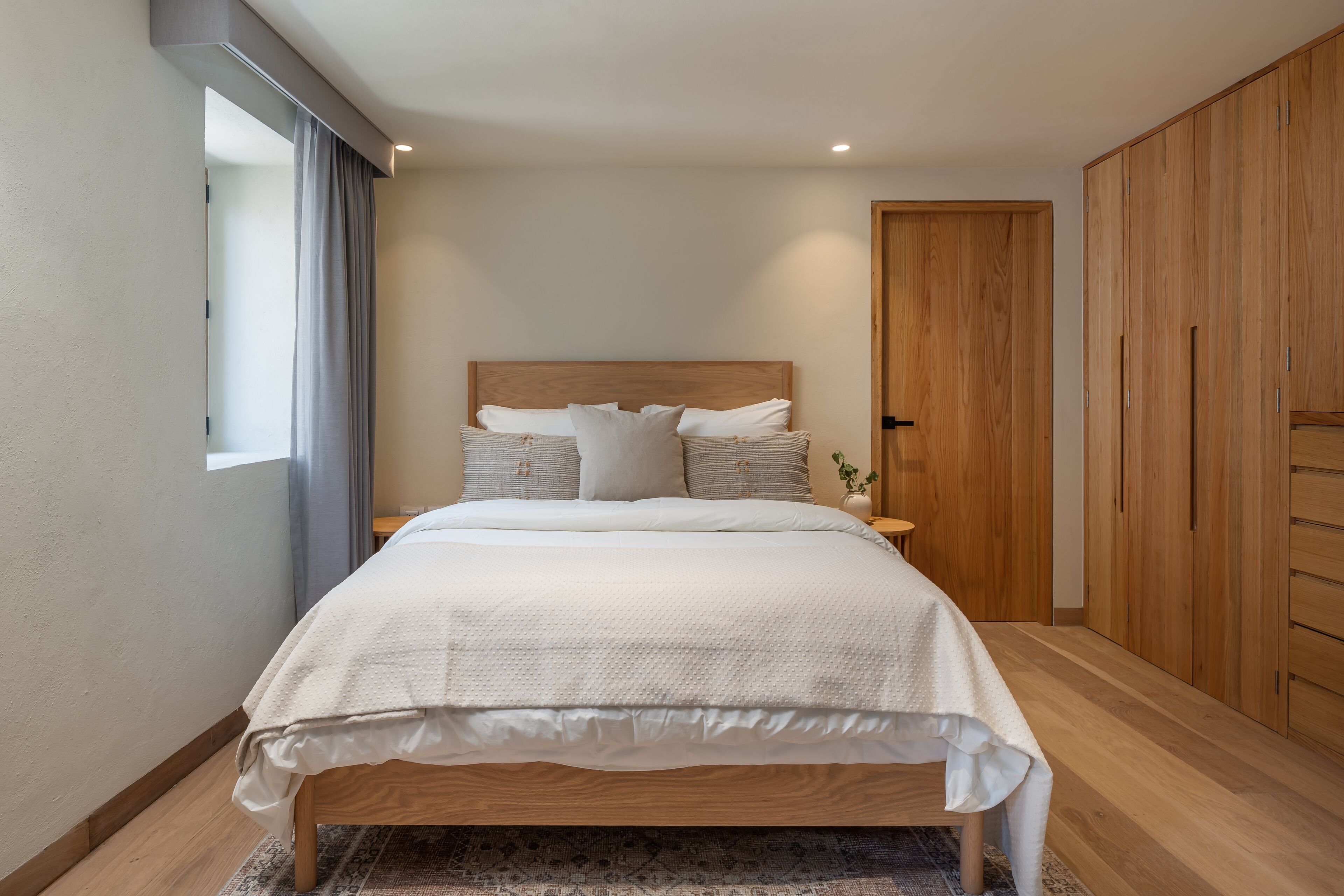 A modern bedroom with a wooden bed, a nightstand, a wooden wardrobe, and a window with curtains.