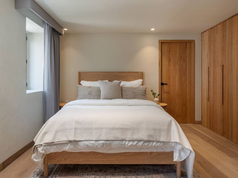 A modern bedroom with a wooden bed, a nightstand, a wooden wardrobe, and a window with curtains.