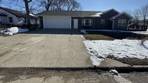Una casa residencial con garaje, entrada para vehículos y césped cubierto de nieve.