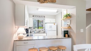 Una cocina con un letrero que dice "BEACH PLACE", un refrigerador, una encimera con una lámpara y tres taburetes de madera.
