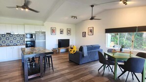 A modern kitchen with white cabinets, a wooden island, and a dining area with a table and chairs. - NEW -The Sugar Shack, Ocean views over cane fields from your outdoor Spa Bath  (Miallo)