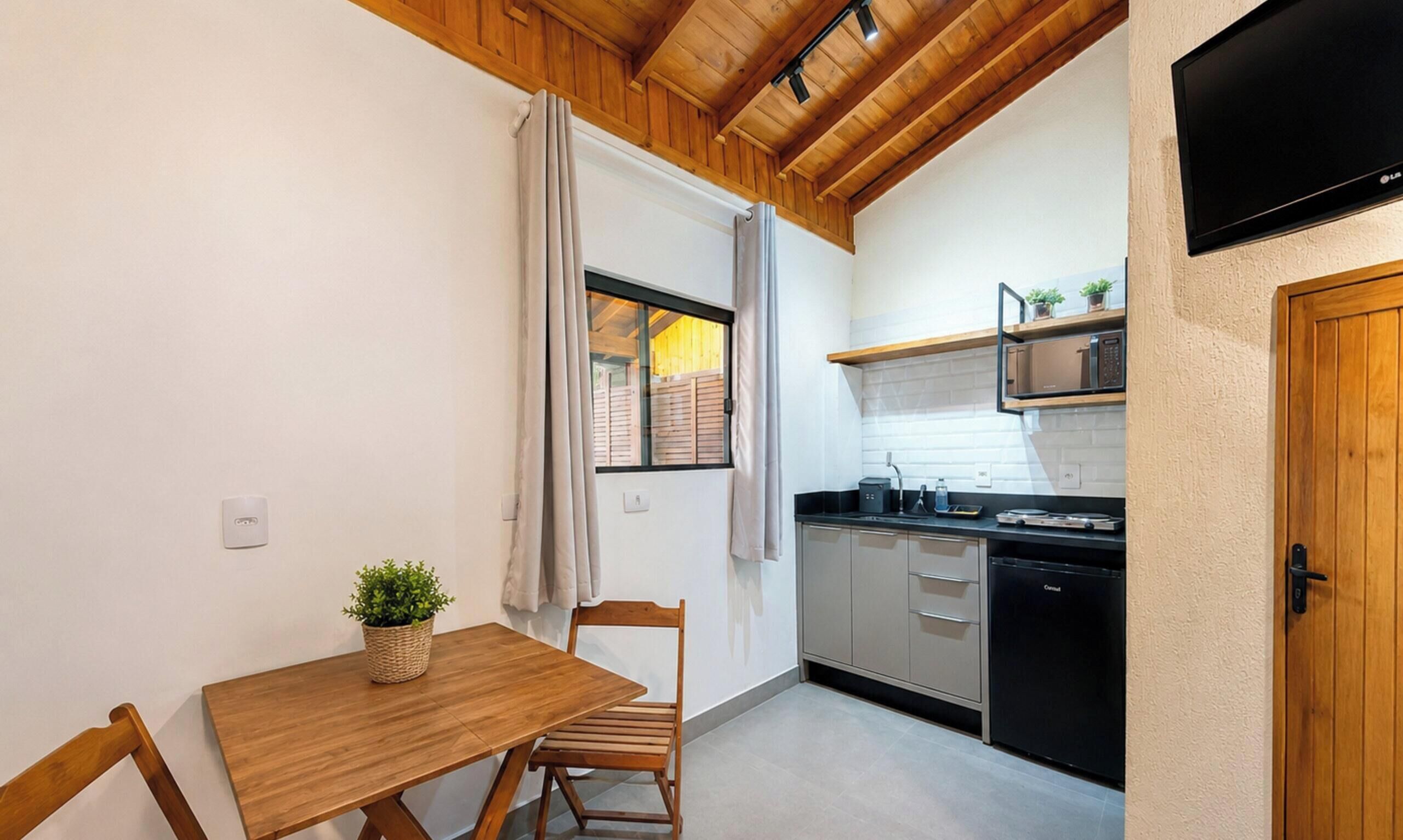 A compact kitchen with wooden ceiling beams, a dining table with chairs, a small potted plant, and a black refrigerator.