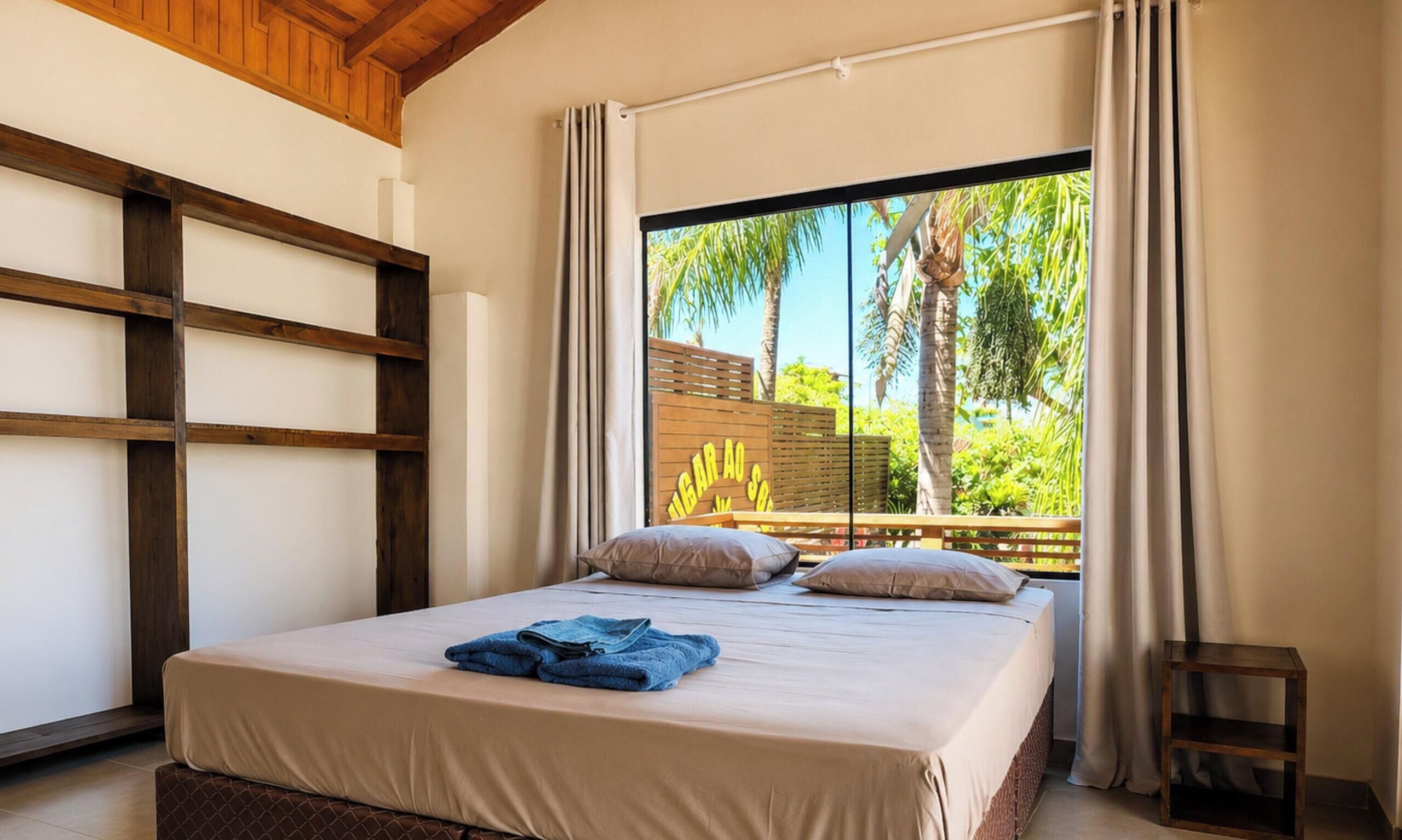 A bedroom with a large bed, a wooden headboard, and a view of greenery outside.