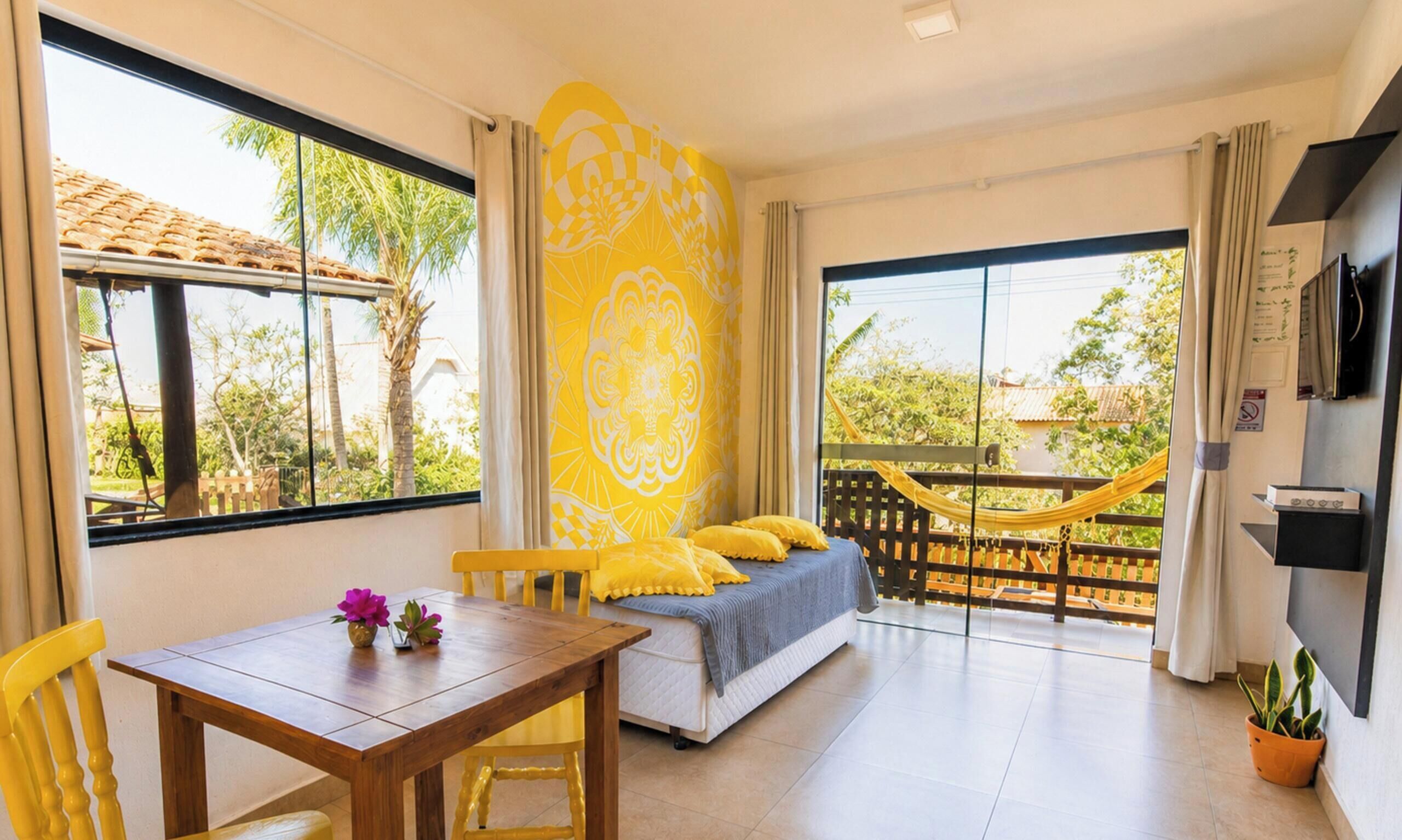 A room with a bed, a dining table, chairs, a hammock, and a TV.