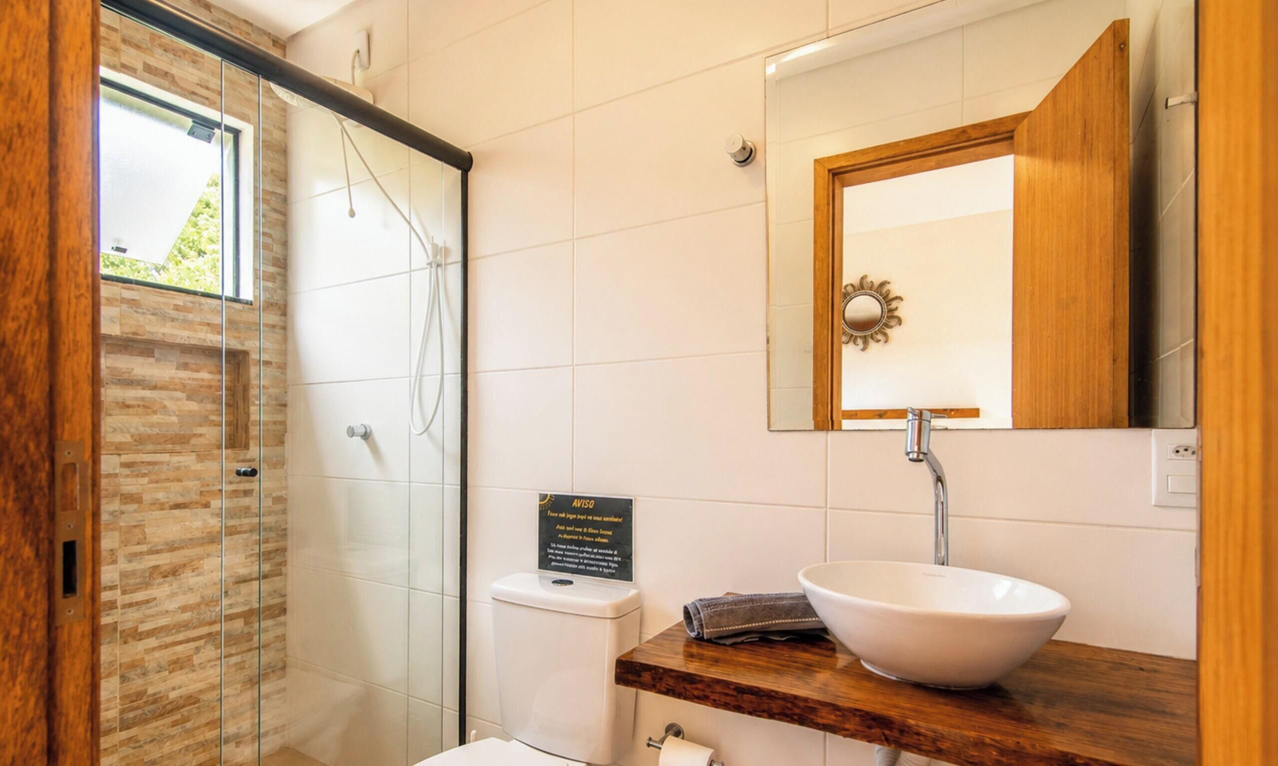 Un baño con cabina de ducha de vidrio, lavamanos blanco y tocador de madera.