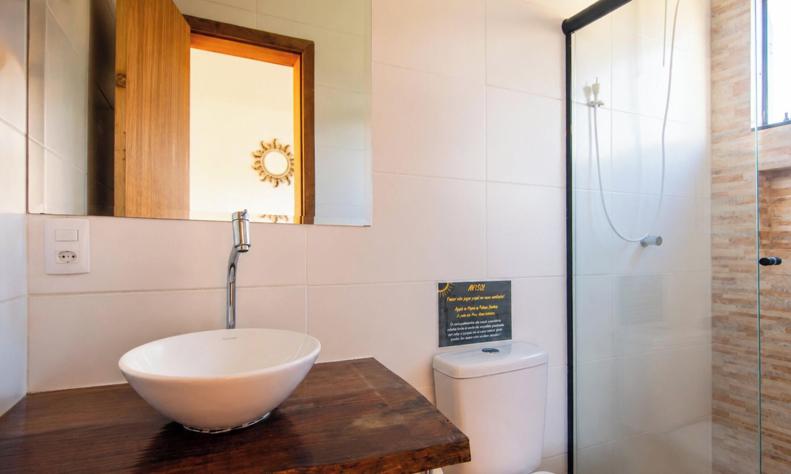 A bathroom with a white sink, a wooden countertop, a mirror, a glass shower enclosure, and a sign with text.
