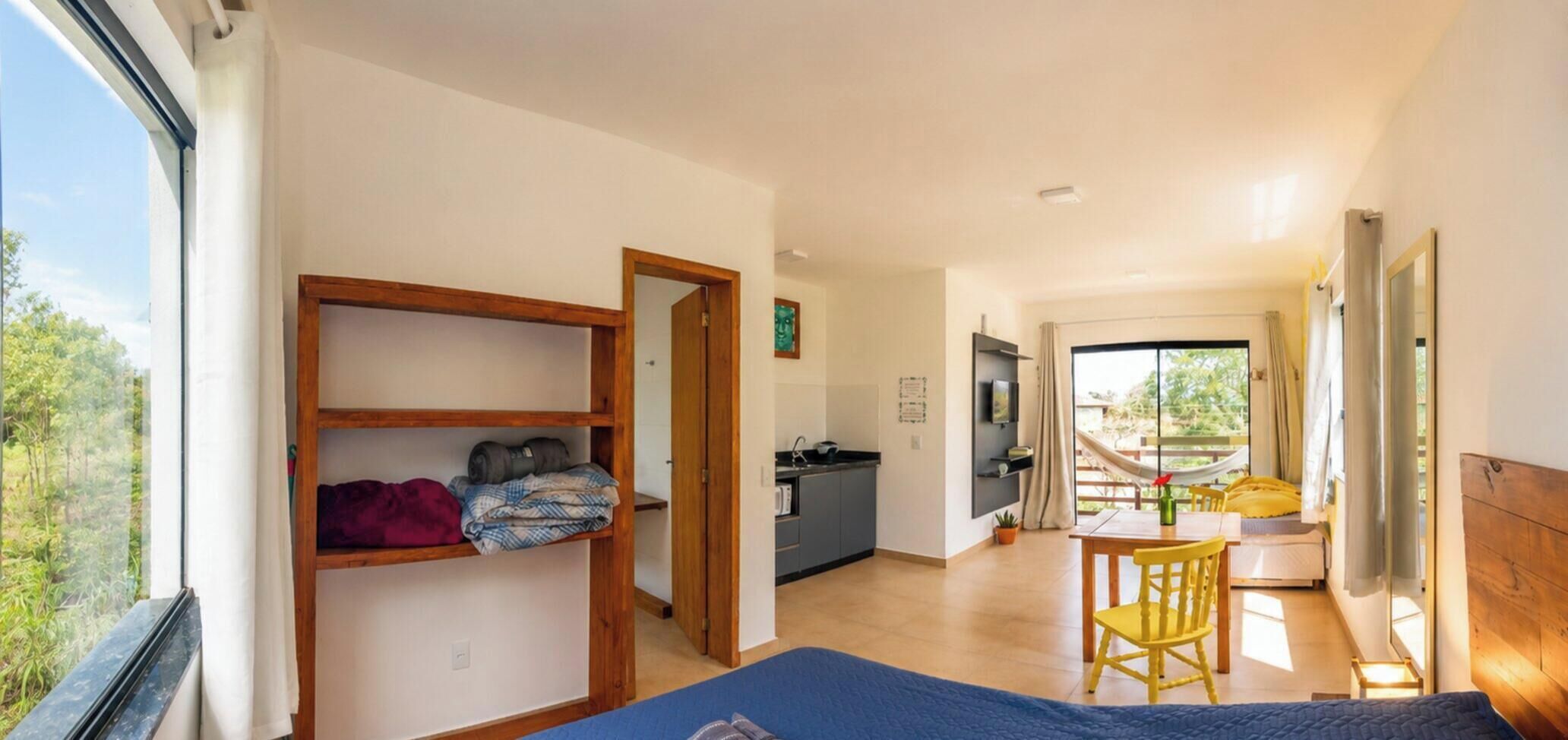 Quarto com cama, escrivaninha, cadeira, janela, porta e vista para o exterior.