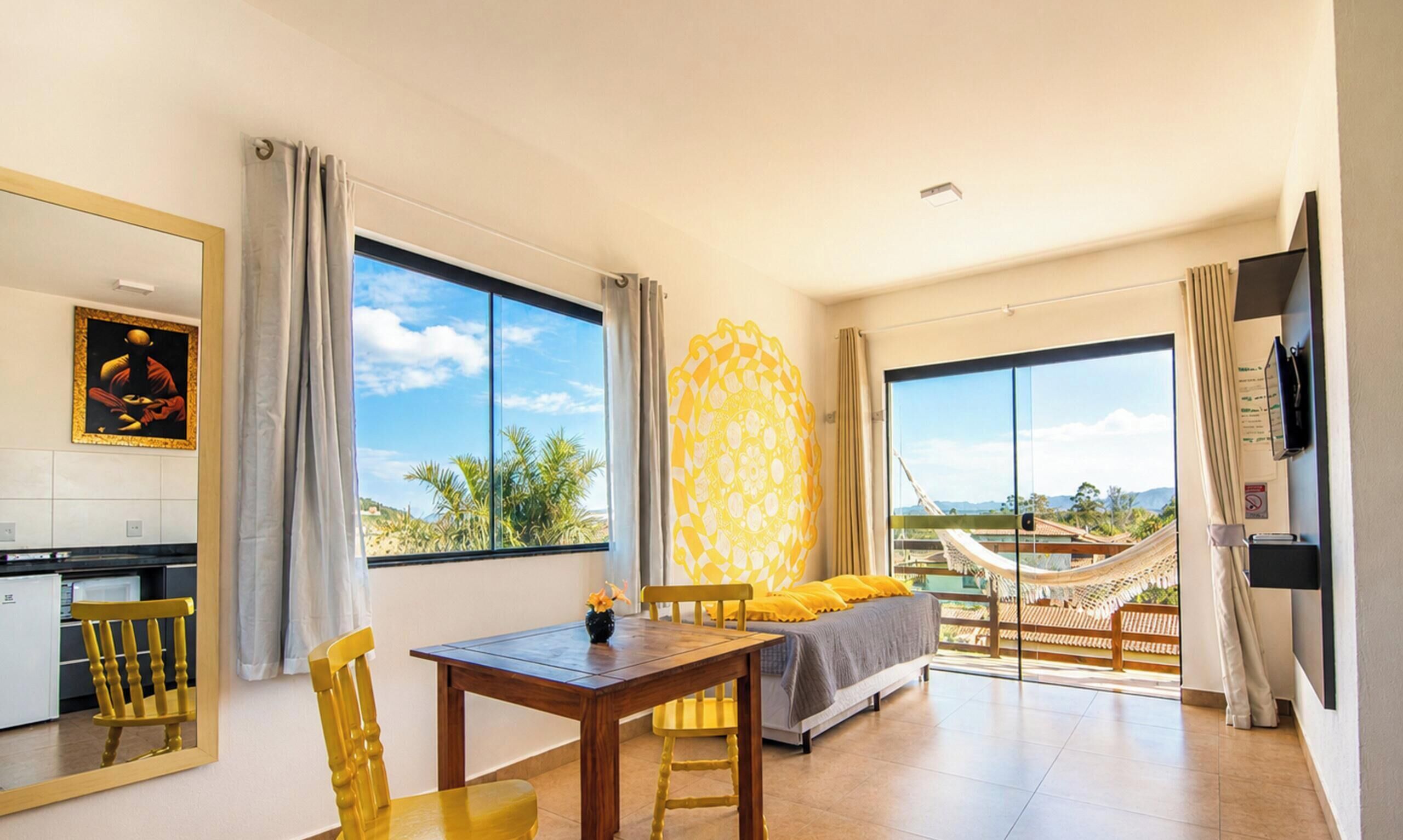Una habitación de hotel con una mesa de comedor, sillas amarillas, un sofá y una hamaca.