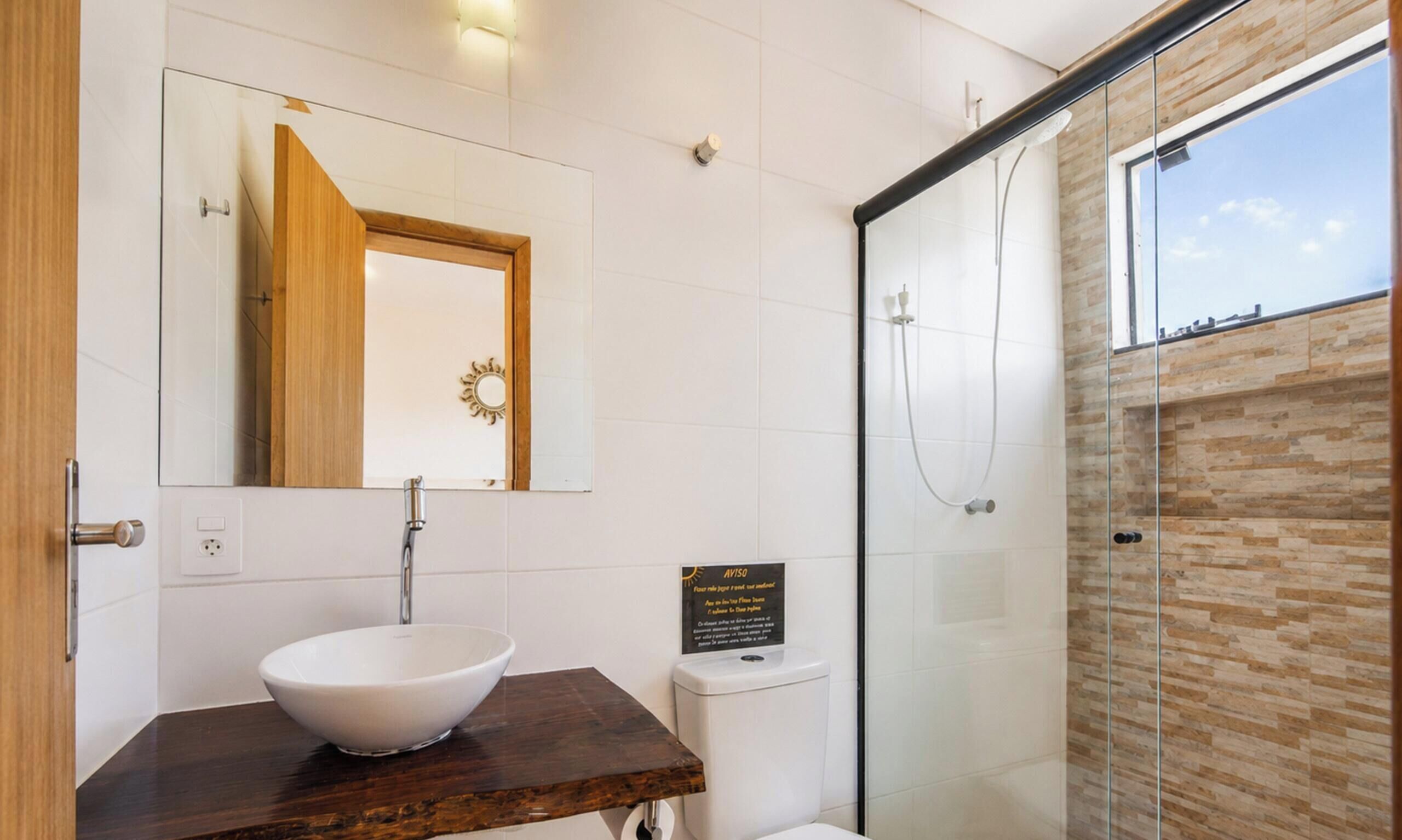 A modern bathroom with a wooden vanity, a white sink, a glass shower enclosure, and a view of the sky.