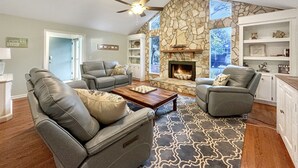 A living room with a stone fireplace, leather sofas, and a ceiling fan.