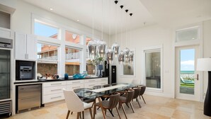 Une cuisine moderne avec une table à manger en verre, des meubles blancs et une vue sur l’extérieur.