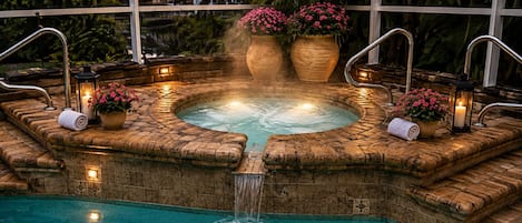 A hot tub with a waterfall feature, surrounded by stone steps and potted plants.