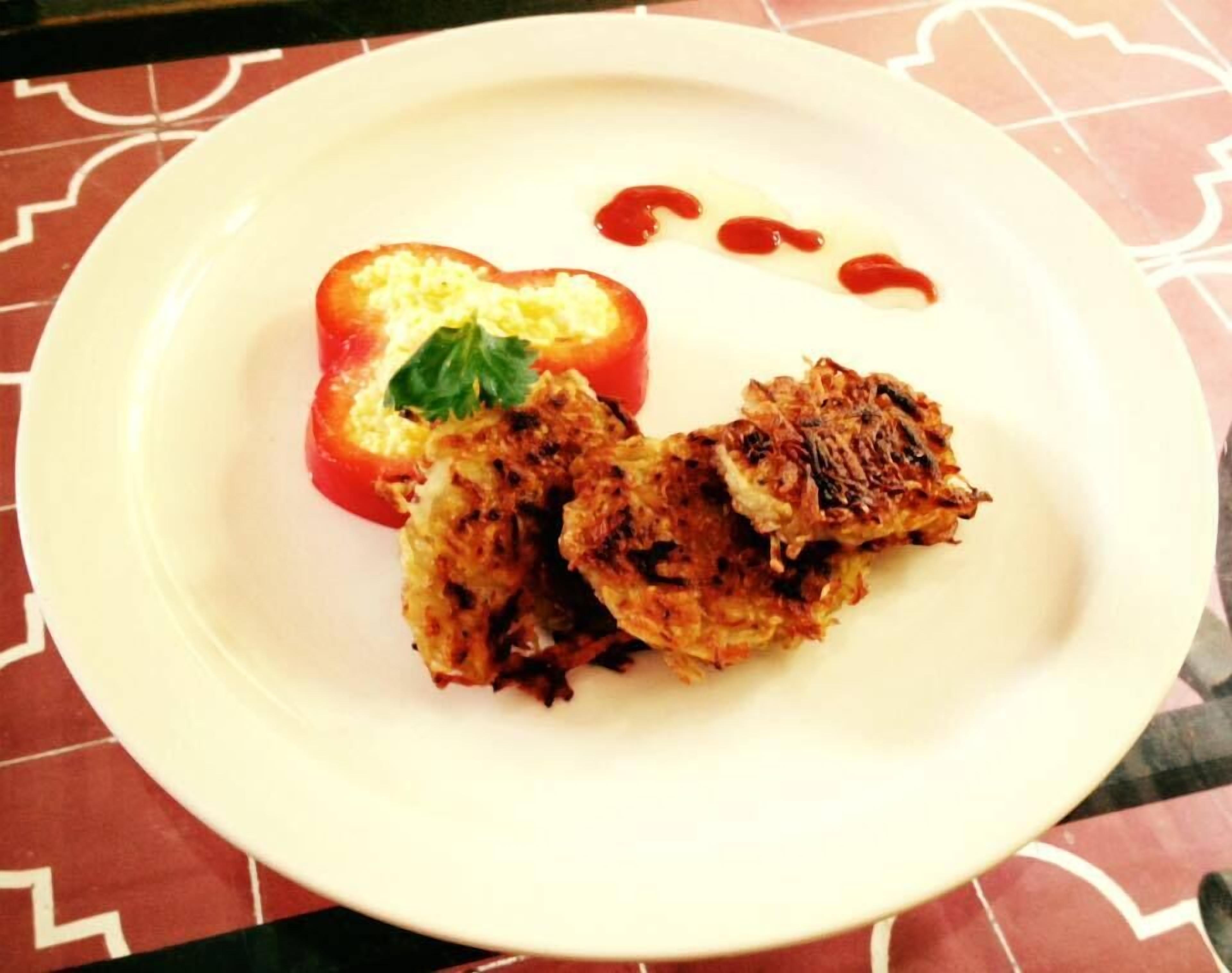 A white plate with a grilled vegetable and a slice of tomato on a patterned tablecloth.