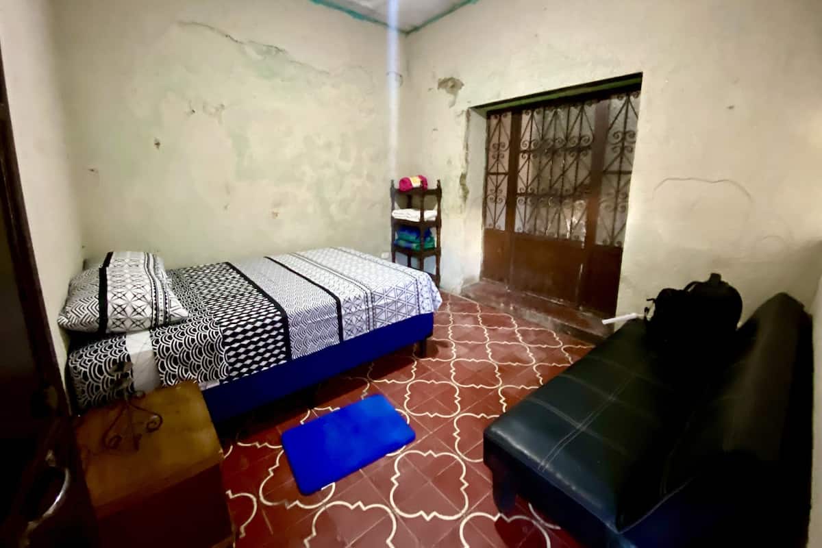 A small, dimly lit room with a single bed, a sofa, and a small table.
