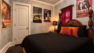 A bedroom with a bed, posters, a door, and a nightstand.