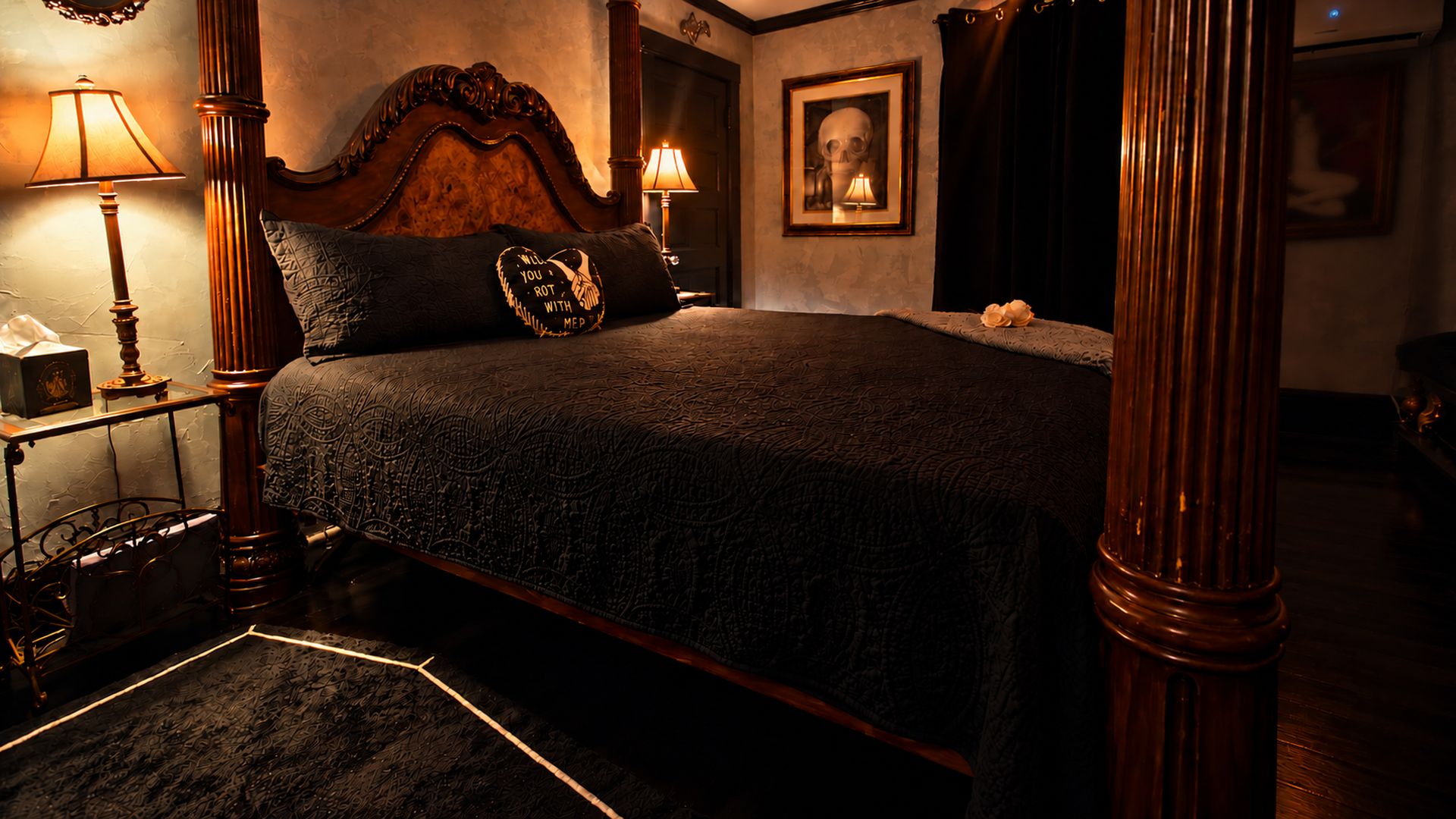 A four-poster bed with a dark, textured bedspread, two bedside lamps, a framed skull artwork on the wall, and a dark curtain.