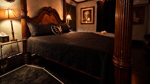 A four-poster bed with a dark, textured bedspread, two bedside lamps, a framed skull artwork on the wall, and a dark curtain. - The vampire's den, downtown big house, pets ok (Fort Smith)