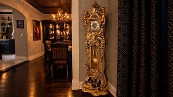 A grand hallway with a large ornate clock, a chandelier, and a dining area with a table and chairs.