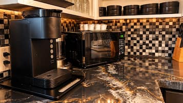 Ett kök med en kaffebryggare, mikrovågsugn och en kakelbeklädd vägg bakom arbetsbänken.