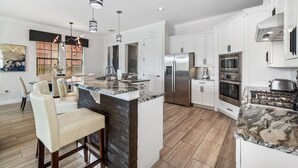 A modern kitchen with white cabinets, stainless steel appliances, and a marble island. - Fairway Evergreen: Theater, Themed Bedroom, Private Pool, Water Park, Near Disney (Kissimmee)