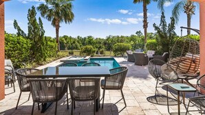 An outdoor pool area with a table and chairs, surrounded by palm trees and greenery. - Fairway Evergreen: Theater, Themed Bedroom, Private Pool, Water Park, Near Disney (Kissimmee)