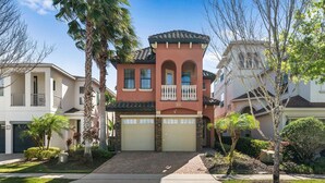 A two-story house with a red facade, a balcony with white railings, and a garage. - Fairway Evergreen: Theater, Themed Bedroom, Private Pool, Water Park, Near Disney (Kissimmee)