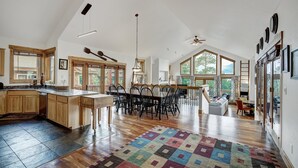 A spacious kitchen with wooden cabinets, a dining area with a large table and chairs, and a living area with a sofa and a TV.