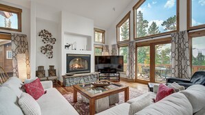 A spacious living room with a fireplace, comfortable seating, and large windows offering a view of the outdoors.