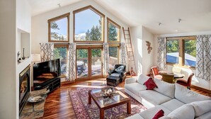 A spacious living room with a fireplace, large windows, and a loft area.