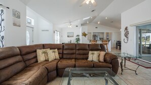 A spacious living room with a large brown sectional sofa, a glass coffee table, and a ceiling fan. - Freshwater Canal, Heated Pool & Brand New Appliances - Villa Seahorse Sanctuary - Roelens (Cape Coral)