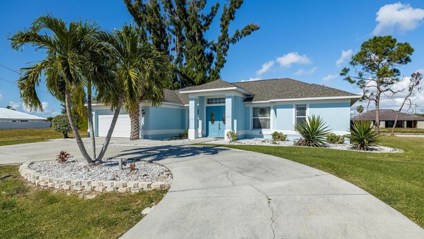 A single-story house with a light blue exterior, a front porch, and a driveway leading to the entrance. - Freshwater Canal, Heated Pool & Brand New Appliances - Villa Seahorse Sanctuary - Roelens (Cape Coral)