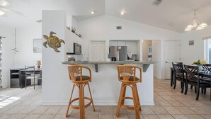 A modern kitchen with a central island, two bar stools, and a dining area with chairs. - Freshwater Canal, Heated Pool & Brand New Appliances - Villa Seahorse Sanctuary - Roelens (Cape Coral)
