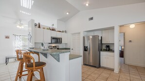 A modern kitchen with white cabinetry, a stainless steel refrigerator, and a bar area with two stools. - Freshwater Canal, Heated Pool & Brand New Appliances - Villa Seahorse Sanctuary - Roelens (Cape Coral)