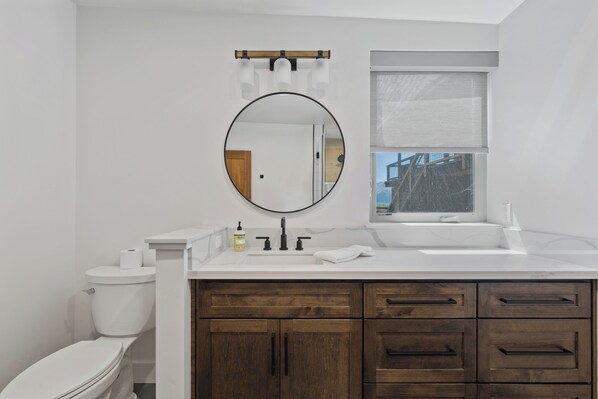Un baño con inodoro, lavamanos, espejo y armarios de madera.