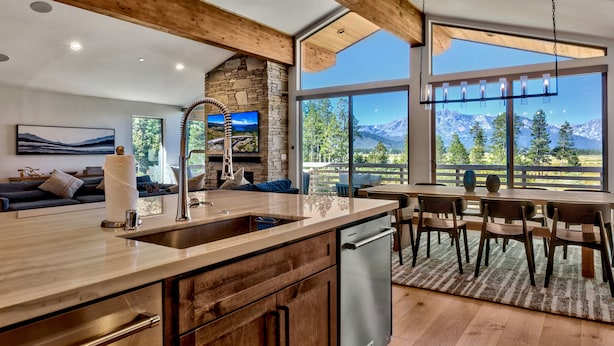 Una cocina moderna con chimenea de piedra, vigas de madera y un amplio ventanal con vistas a un paisaje montañoso.