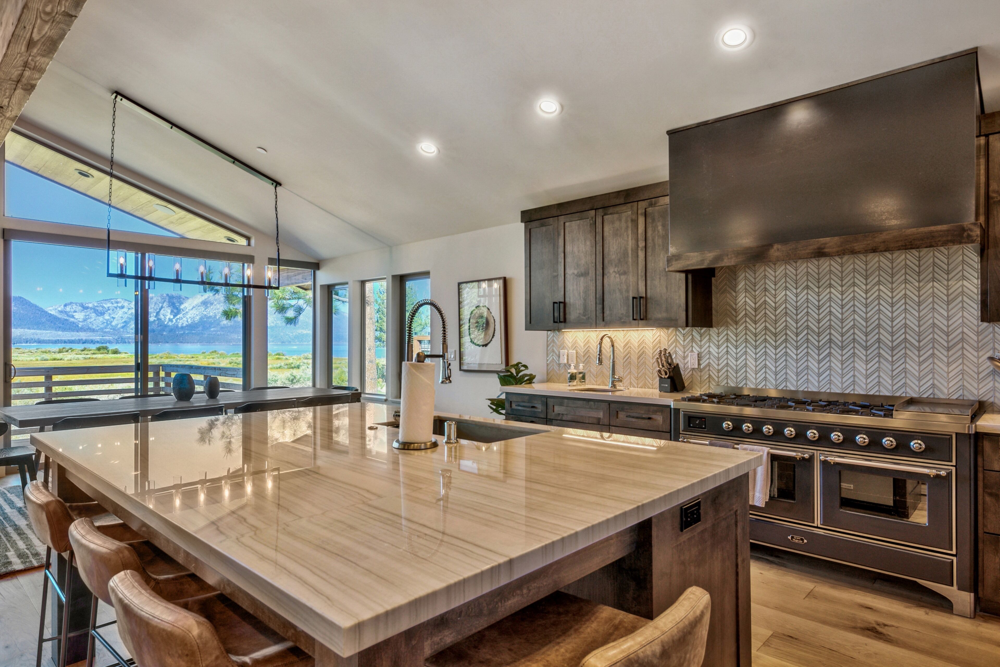 A modern kitchen with a large island, stainless steel appliances, and a view of mountains.